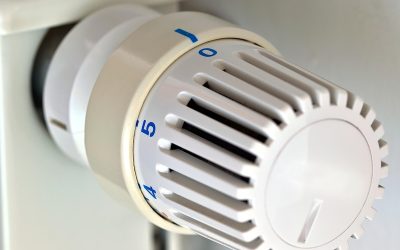 Un thermostat mural avec une main qui tourne le cadran pour régler la température