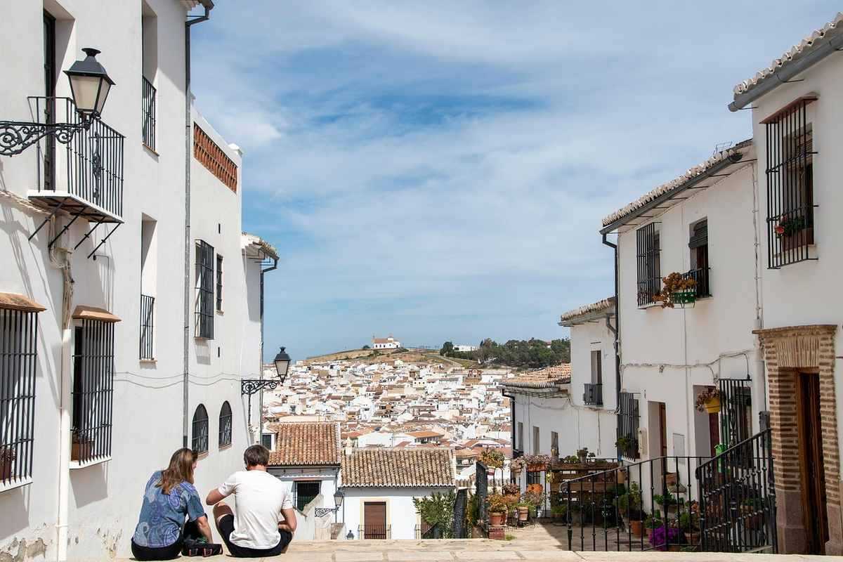 Deux touristes assis observent un village blanc avec toits de tuiles ocre et maisons blanches en terrasse sous ciel bleu
