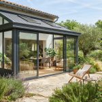 Véranda moderne en aluminium accolée à une maison, baies vitrées, jardin ensoleillé